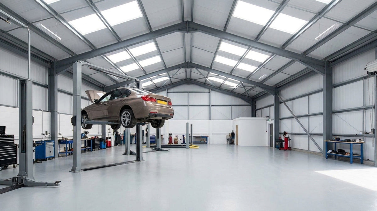 Spacious UK workshop with a car raised near full height on a two-post lift showing headroom