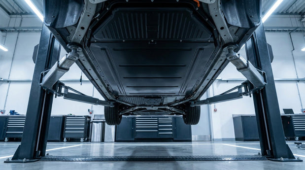 Electric car raised on a two-post lift showing the flat battery pack across the underside